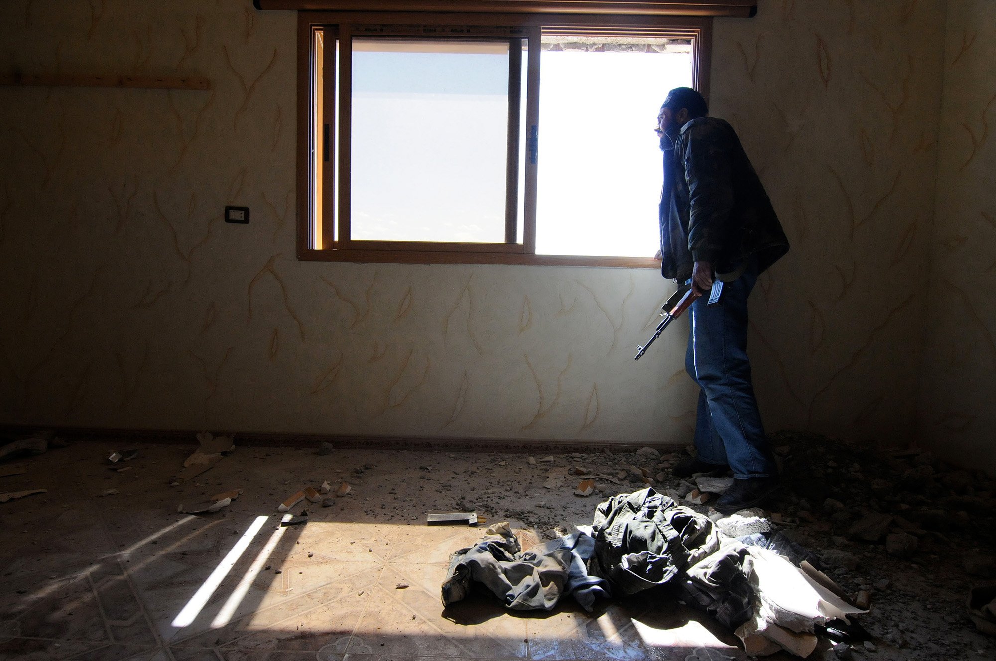 Un combattente dell'FSA è alla ricerca dall'interno di una posizione difensiva dopo che le forze governative hanno appena bombardato l'area con carri armati 80 km a nord di Damasco - Siria, 25 aprile 2013, di Jonathan Alpeyrie