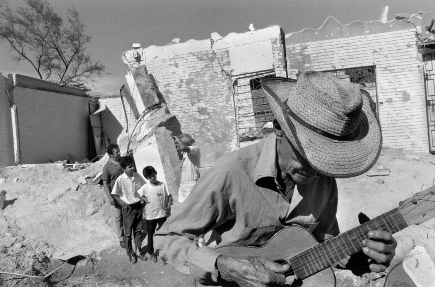 Ein Mann spielt Gitarre in einem Viertel in El Salvador, in dem Guerillas Zuflucht suchten und Regierungstruppen zivile Häuser zerstörten. El Salvador, 1989 © Larry Towell