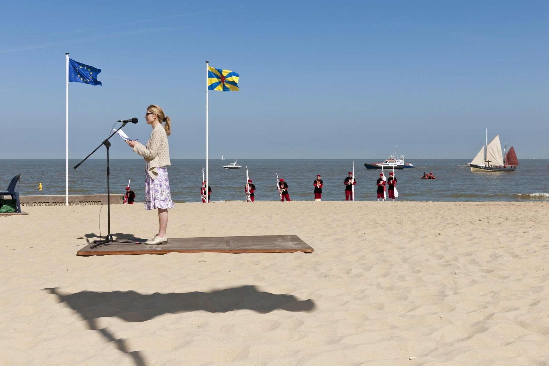 Fotografia di strada a colori di donne che danno un discorso sulla spiaggia con bandiere di Nick Hannes