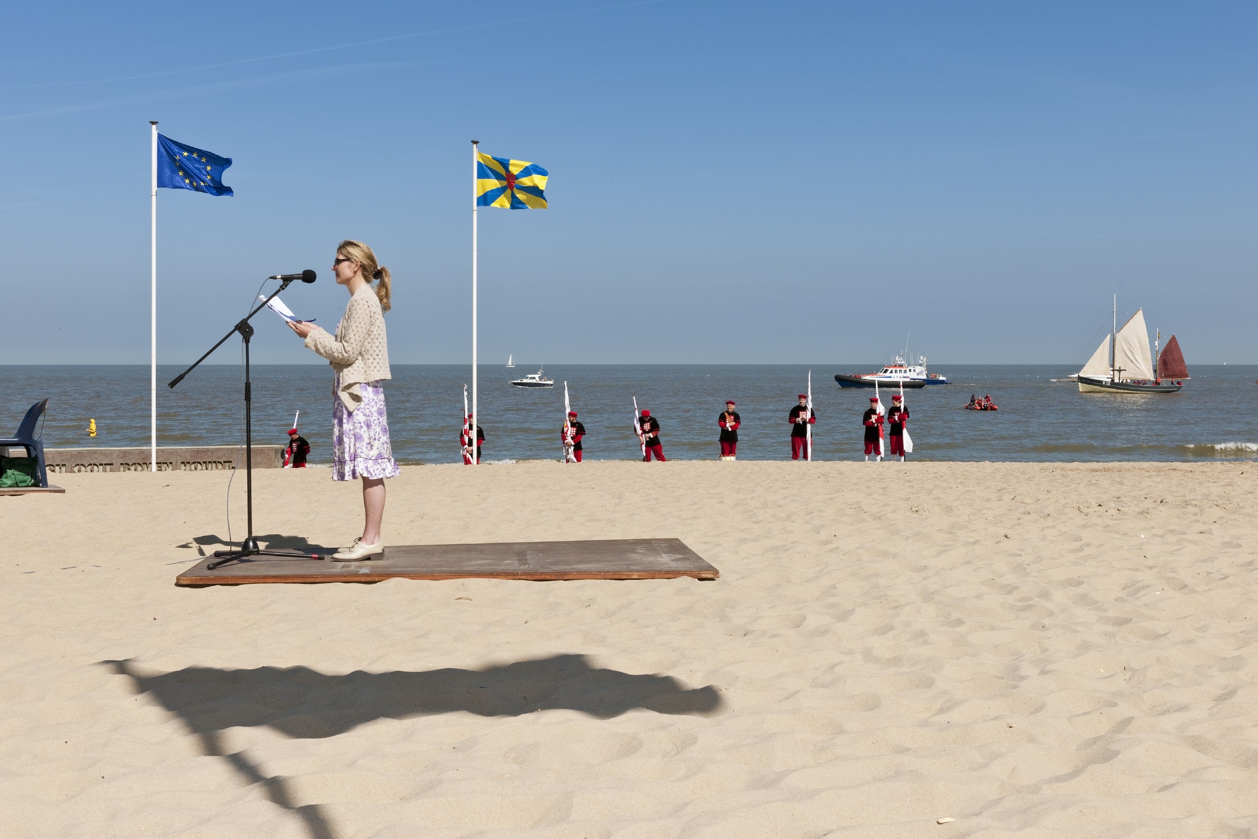 Fotografía de la calle en color de mujeres dando un discurso en la playa con banderas por Nick Hannes