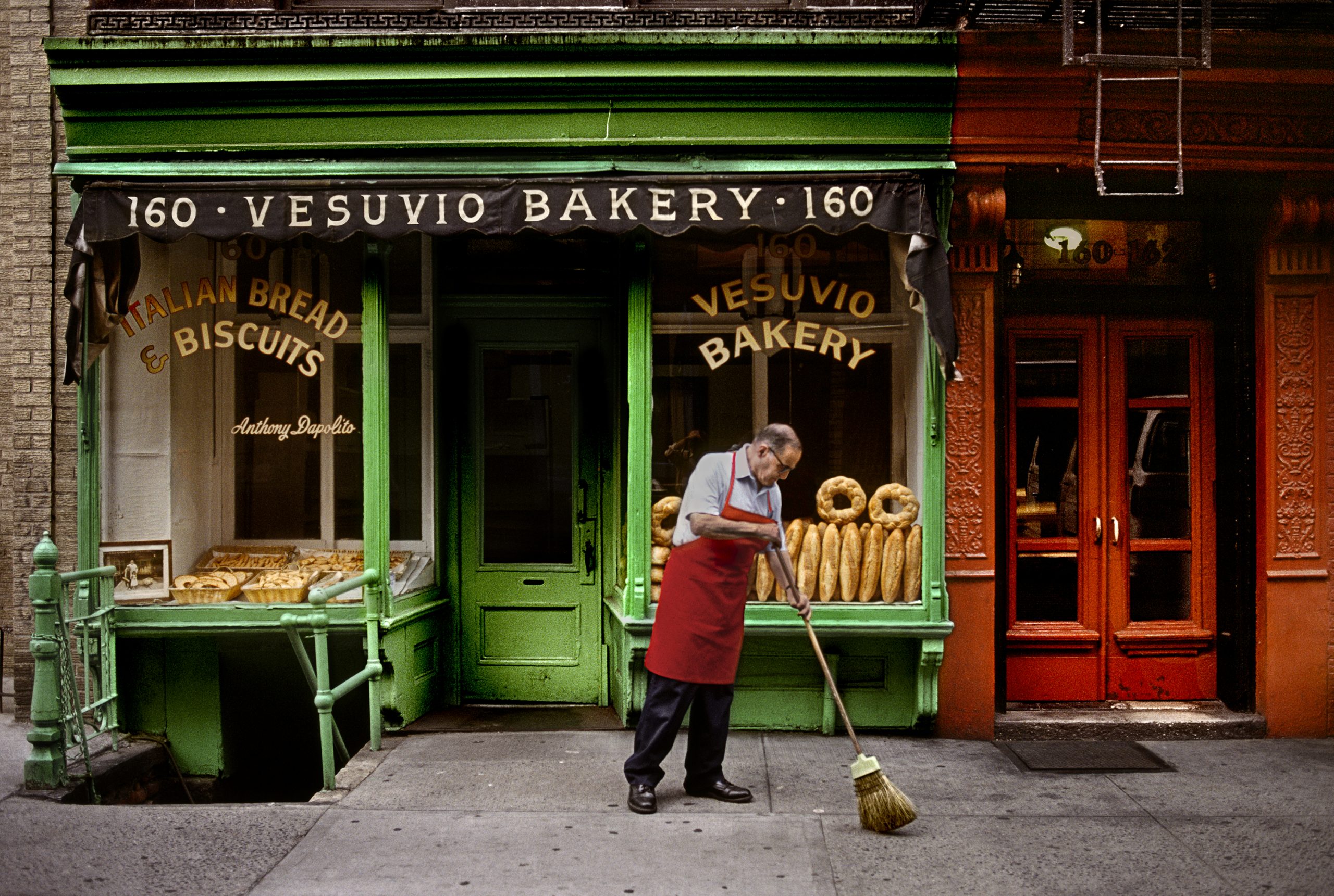 美国纽约市史蒂夫·麦卡里(Steve McCurry)的彩色照片,在意大利面包店外的大街上清扫的人。