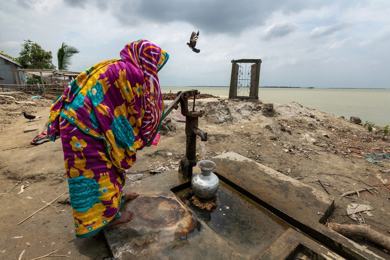 Color photograph of a woman collecting water on eroded land in Bangladesh - Visual Storytelling Award