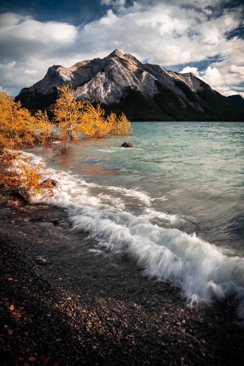 color landscape photograph of waves lap against the shore of Abraham Lake, Alberta Canada in autumn,