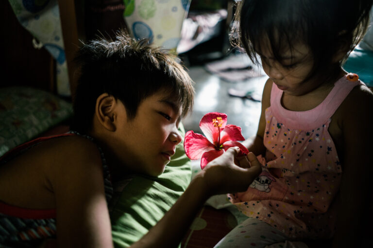 Un jeune garçon touche une fleur de gumamela que sa sœur a cueillie sur le sol. Ils vivent dans un immeuble à Manille où de nombreux décès liés à la drogue ont eu lieu. Photographie documentaire couleur par Hannah Reyes Morales, de la série "Season of Darkness". Visual Storytelling