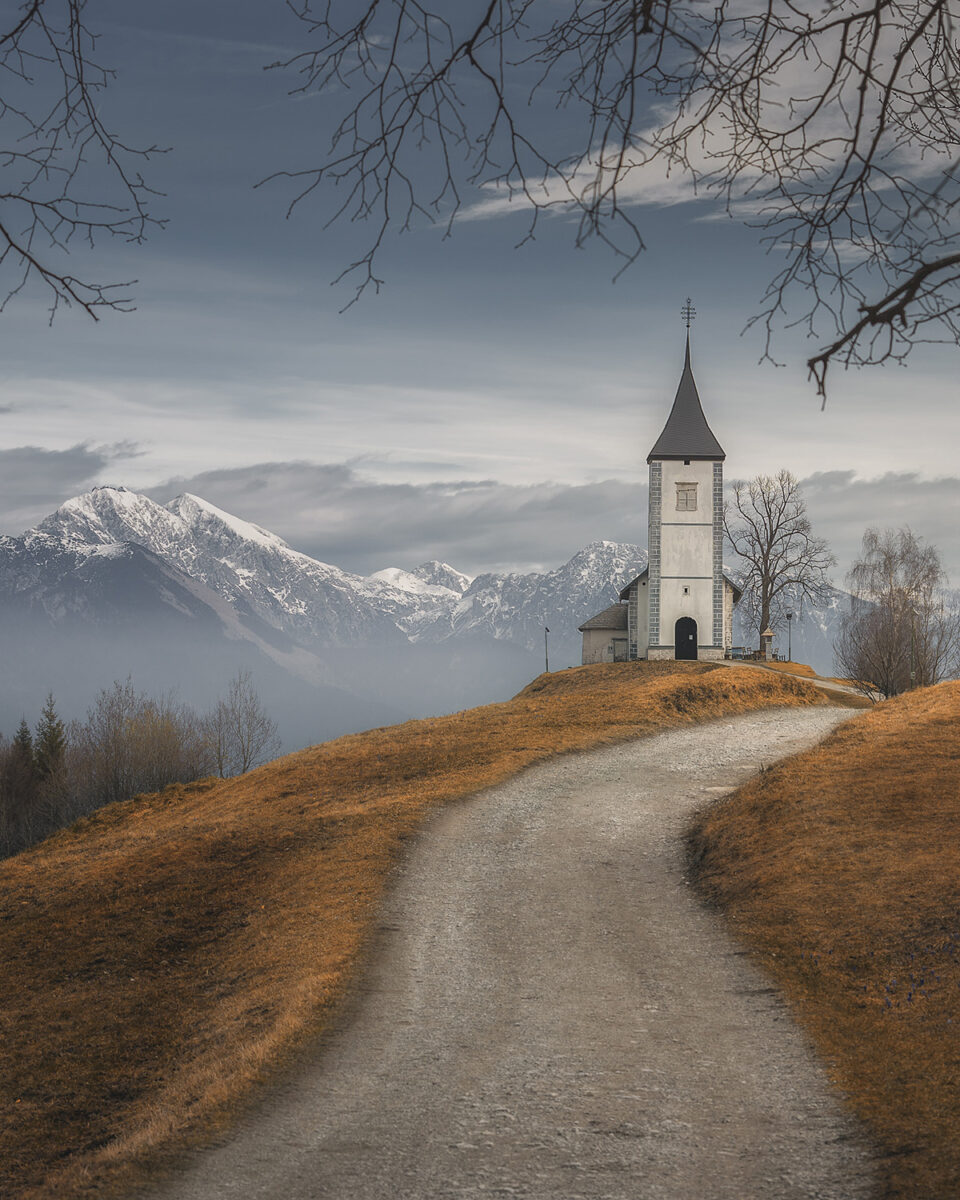 color landscape photo of a church and mountains in Slovenia by Thomas de Franzoni