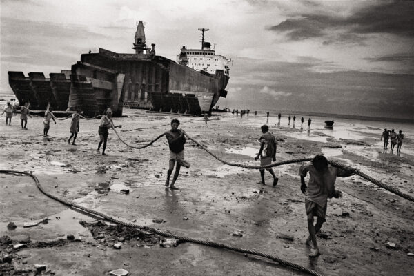 Black & white photography by Ian Berry. Bare-handed men and boys prepare to drag a hawser in the ship-breaking yard. Huge tankers are driven at full throttle and high tide on to the beach where they are broken up mostly by hand with scant regard for health and safety. in Bangladesh