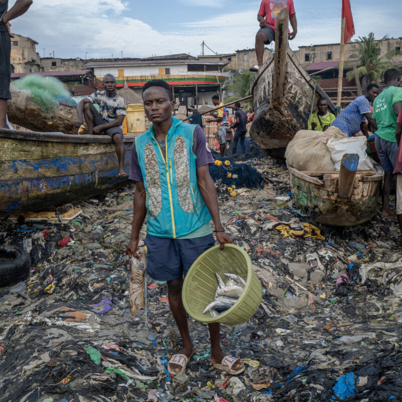 Photography by Kasia Trojak. Fishermen on a beach covered in clothing waste in Accra, Ghana.