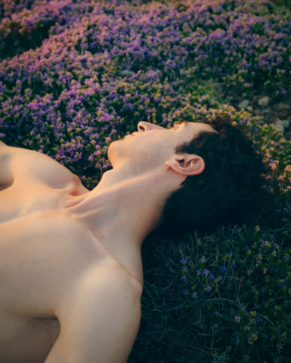 Color portrait photo of man laying on flowers by Kuba Świetlik