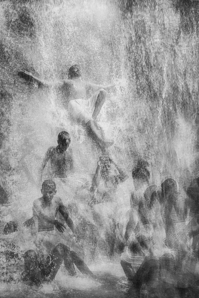 Black and white multi exposure photo of people bathing under waterfall in Kerala, India by Antonio Carreira