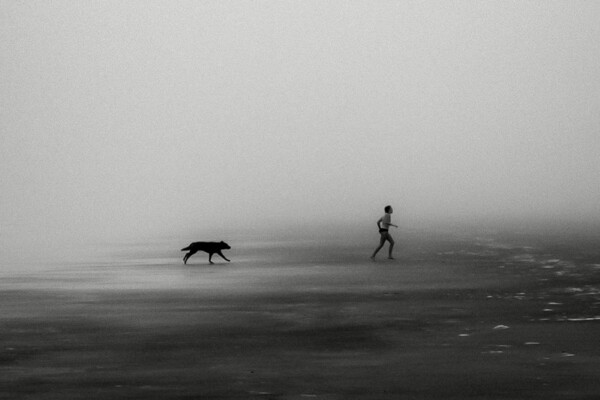 Black and white photo of bpy and dog running on misty beach Jekyll Island, Georgia, USA by David Royds