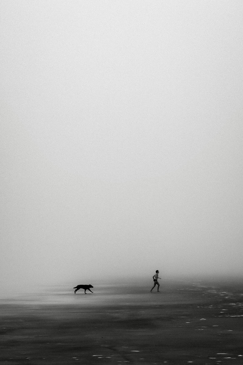 Black and white photo of bpy and dog running on misty beach Jekyll Island, Georgia, USA by David Royds