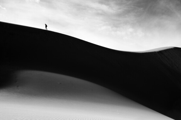 Black and white photo of man walking at Great Sand Dunes, Colorado, USA by William Cunningham