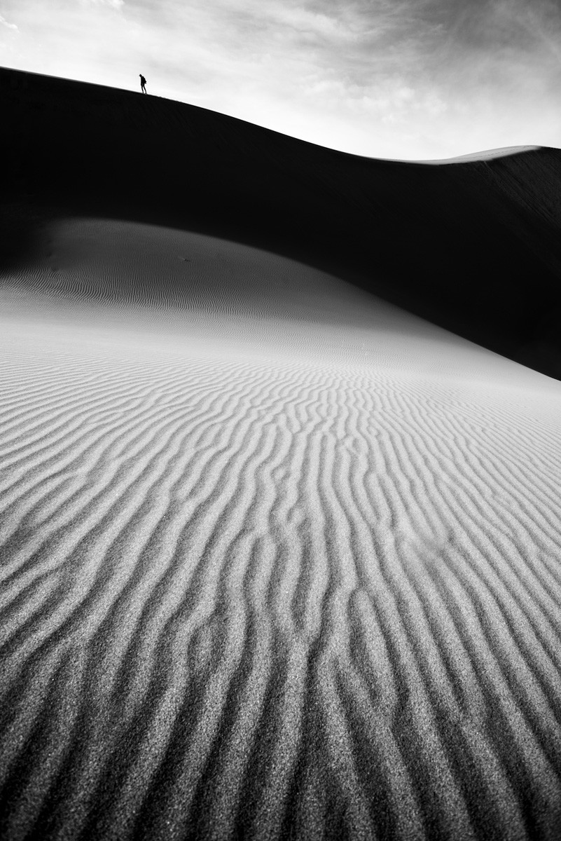 Black and white photo of man walking at Great Sand Dunes, Colorado, USA by William Cunningham