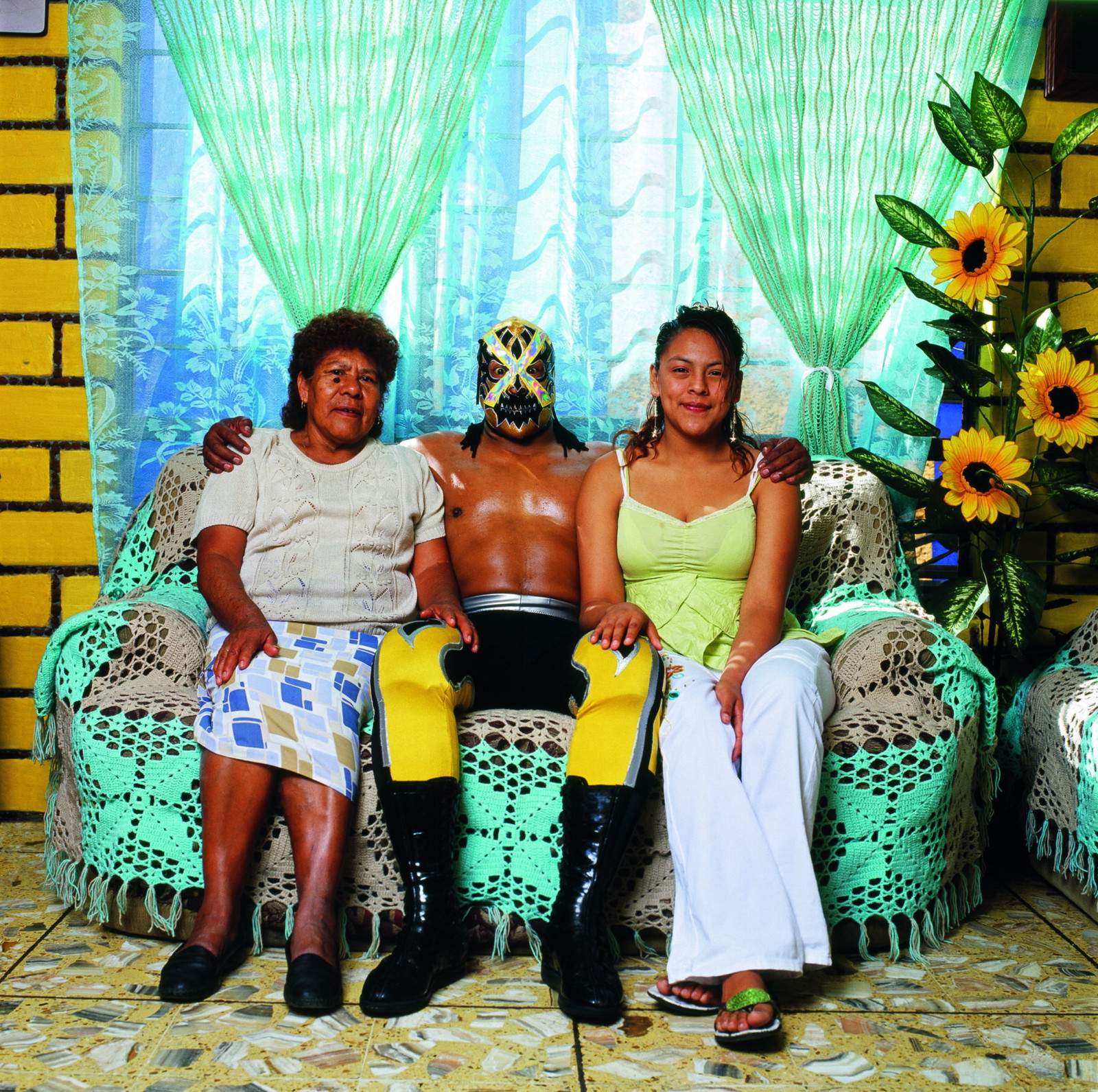 Portrait of Lucha Libre wrestler in his mask sat with his wife and mother at home by Lourdes Grobet