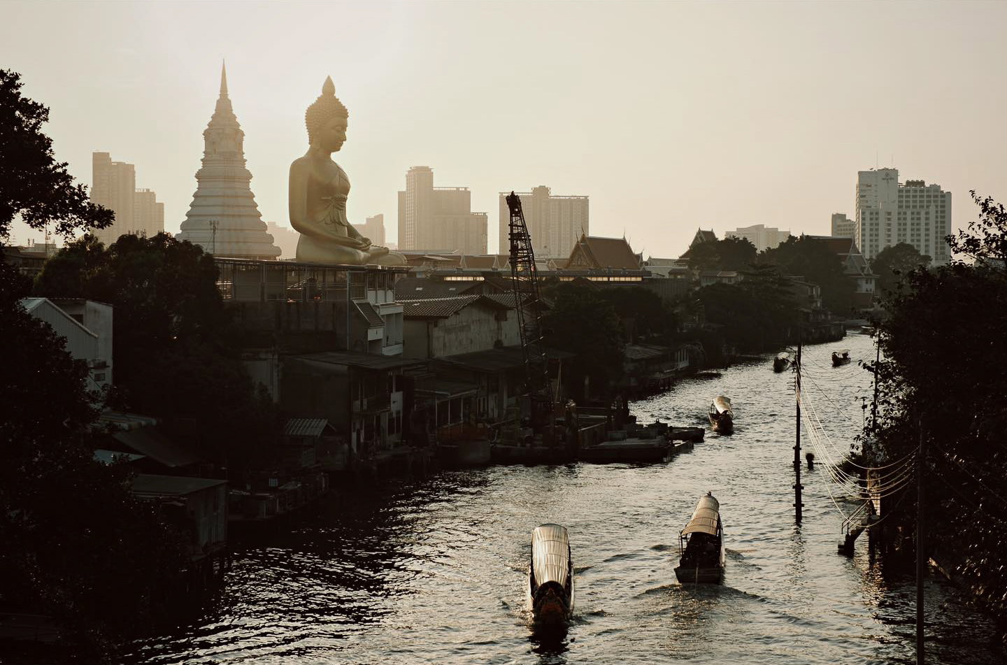 Travel photography by Gil Kreslavsky. Boats on a river with a large buddha statue and temples in the background