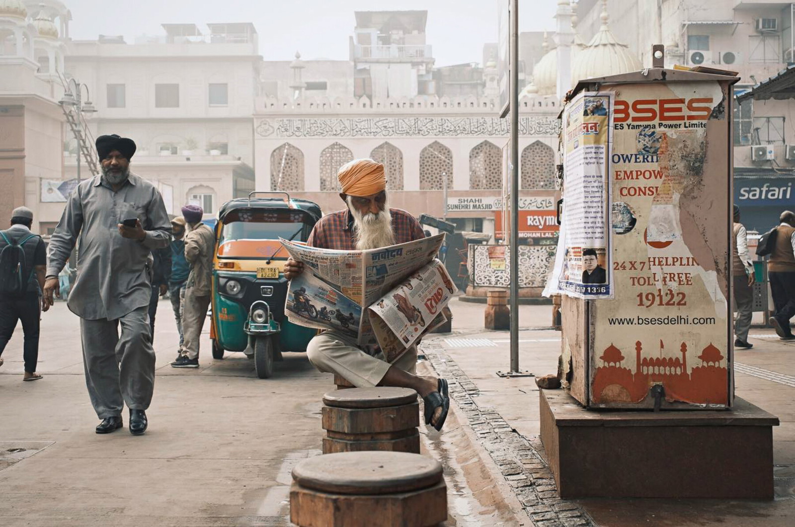 Travel photography by Gil Kreslavsky. A man in an orange turban reading the newspaper on the street in India