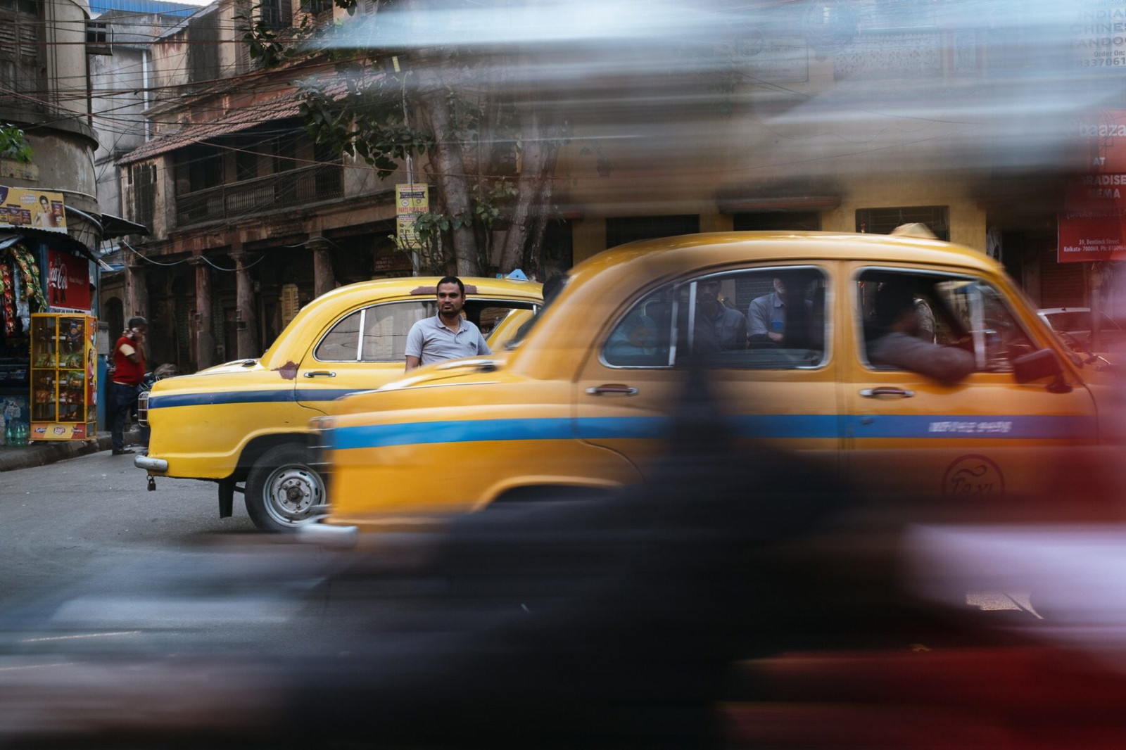 Street photography by Gil Kreslavsky. Taxi driver in front of yellow taxi, India
