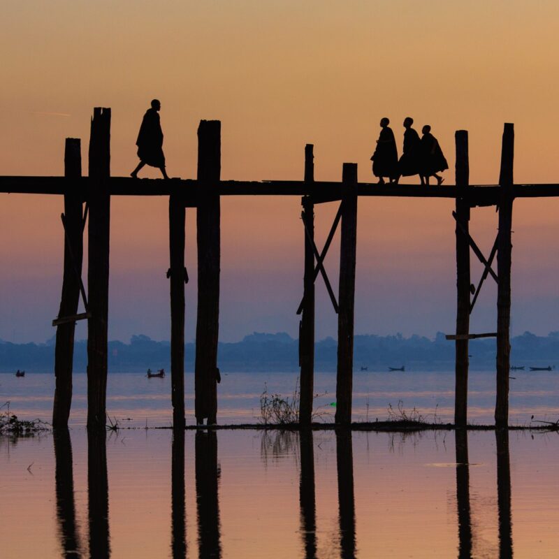 Travel photography by Gil Kreslavsky. Monks crossing a bridge a wooden bridge at sunset