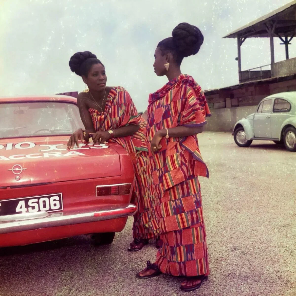 Color portrait of two women in traditional red patterned dress next to a red car in Accra, Ghana