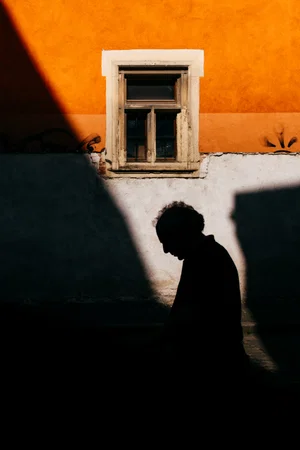 Color street photo of man's shadow against bright orange wall by Mihail Onaca