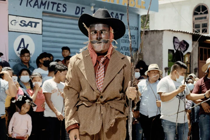 Documentary photography by Juan Brenner. Portrait of a man in a mask with people behind him in Guatemala
