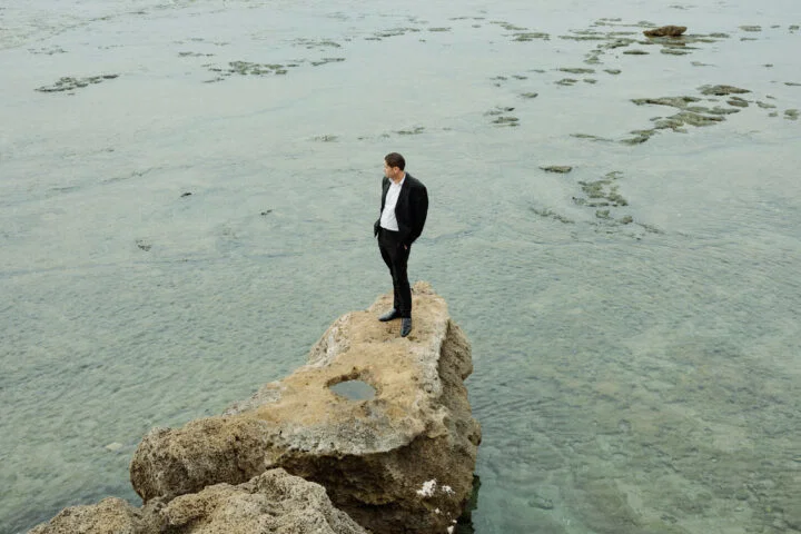 Portrait of a man stood on a rock in front of the sea by Vedad Divovic