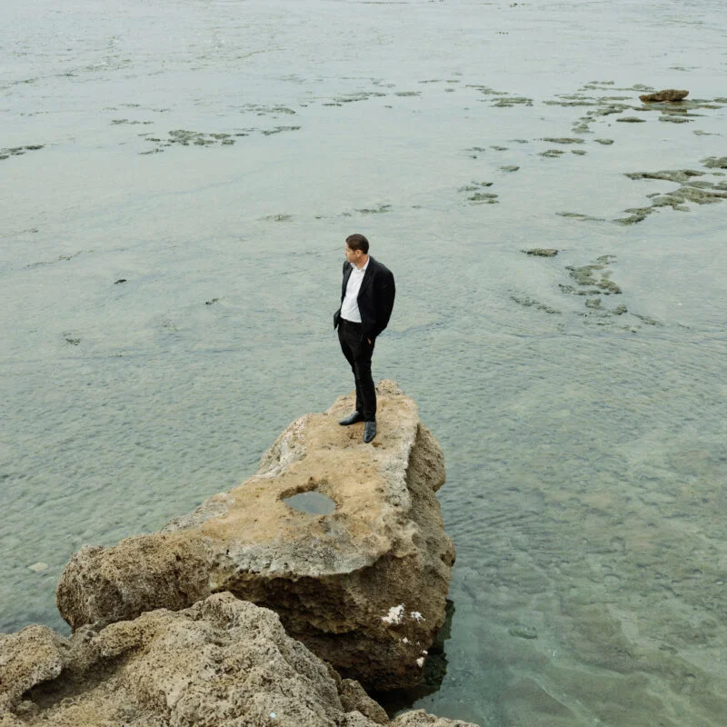 Portrait of a man stood on a rock in front of the sea by Vedad Divovic