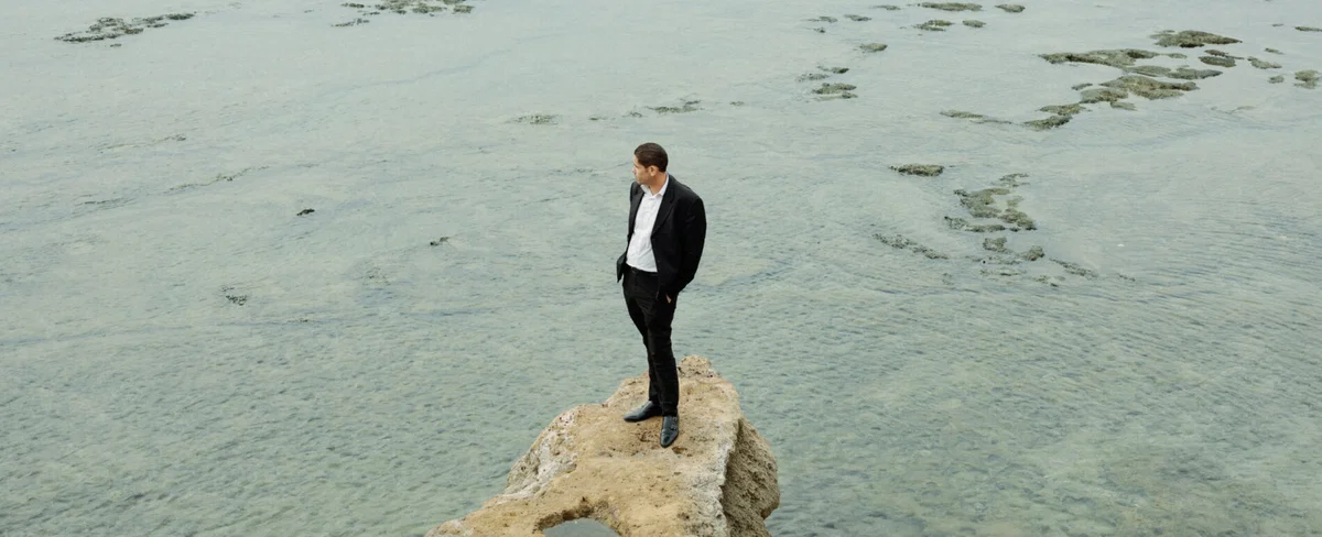 Portrait of a man stood on a rock in front of the sea by Vedad Divovic
